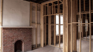 Professional photo of new wood studs, original wood floor, original rough brick bearing walls, wood rafters above, and the second brick fireplace.