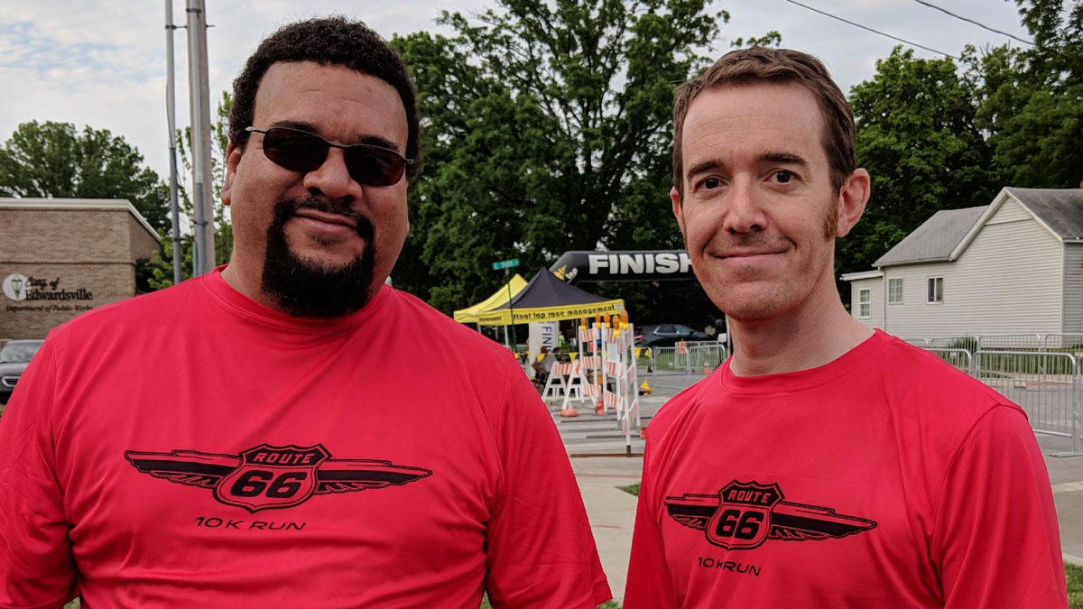 Eric and Ryan, REspace Co-founders in their red route 66 10k volunteer shirts. Photo is full frame with small amounts of the race finish line in the background visible.