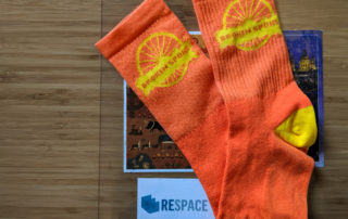 A photo of the bright orange cycling socks with the Broken Spoke logo in yellow on the ankle given away for participating in the Broken Spoke Brew Ride.