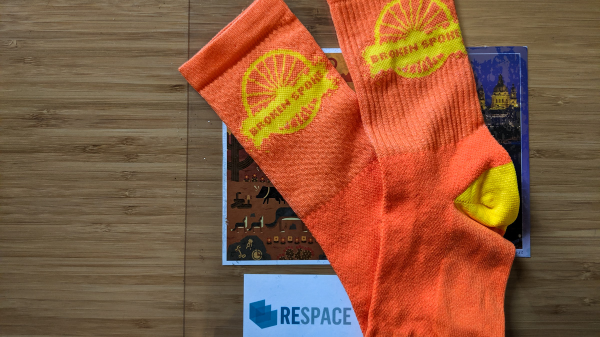 A photo of the bright orange cycling socks with the Broken Spoke logo in yellow on the ankle given away for participating in the Broken Spoke Brew Ride.