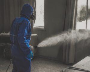 Person in hazmat suit misting room with antimicrobial mist