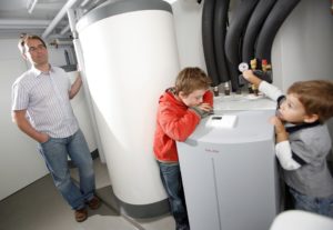 A man supervises two children who are looking at a basement electric heat pump water heater.