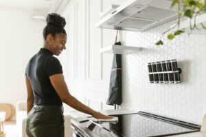 A smiling Black woman prepares to use an electric stove by first wiping it clean with a towel.
