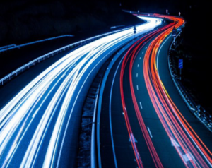 An electrified highway at nighttime is depicted, ith red or blue lines simulating the paths of electric vehicles.